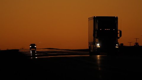 Dawn traffic with orange sky. Semi truck approaches and passes, with pickup truck in the distance. Saskatchewan, Canada. 