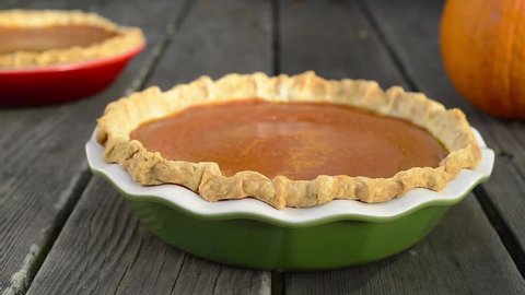 Slider shot of two pumpkin pies and a small pumpkin on weathered wood boards.  Green and red ceramic pie plates. : vidéo de stock