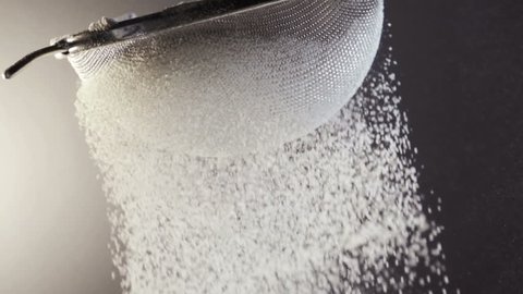 Close up of a fine curtain of refined white cake flour falling through a metal sieve in a kitchen while cooking a recipe