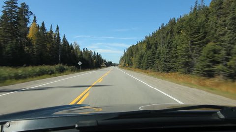 Sunny drive with conifers on either side of the highway. Approaching a rockcut. Driving on HWY 17, close to Cigar Lake in Northern Ontario, Canada.