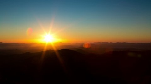 Time lapse of the sun rising from behind mountains. A beautiful lens flare moves through frame.
