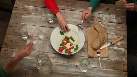 Eating Caprese salad with friends in rustic style - stop motion animation of salad preparation and timelapse of eating, 4K, top view (closeup shot from another angle also available)