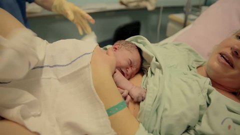 Nurse put number on a born baby and mom. Mother is crying after looking her baby for the first time while baby is crying just after birth with blood on him