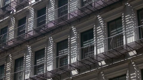 Sun hitting a New York City apartment building, casting striped shadows through the steel balconies. Close shot.