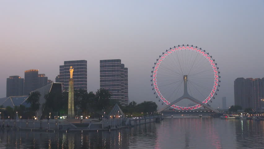 Panoramic view of Tianjin Eye, Ferris wheel in public park in twilight, Chinese cityscape at sunset