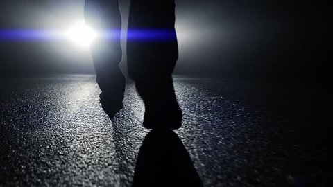 camera following feet walking towards car light beams in dark night. foot steps close up
