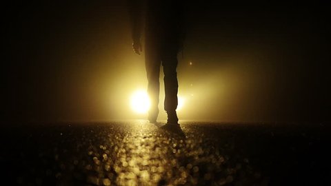 low angle view of man feet walking into dark night. mystical fog background. light beams