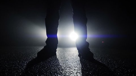 backlight silhouette of mystery man standing in front of car light beams
