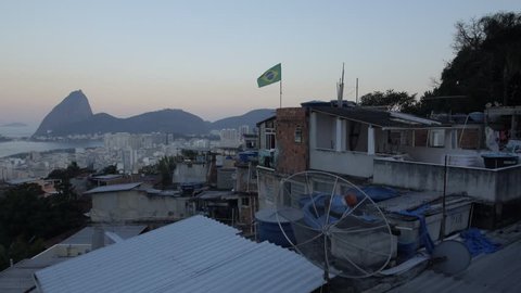 Aerial favela flight over Brazil flag waving in wind with Sugarloaf Mountain in the background