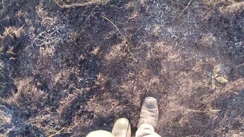 legs in boots walking on the burnt grass top view in the first person