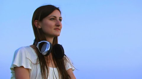 The girl in headphones on the skyline. She wears big headphones and listening to music on the background of a beautiful blue sky.