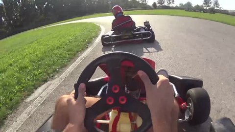 two drivers  drive go kart and overtaking on outdoor track, camera is attached to the helmet
