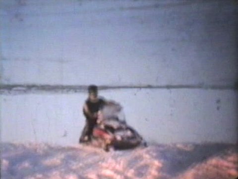 Two snowmobiles do some spins on a frozen river while out having fun snowmobiling.