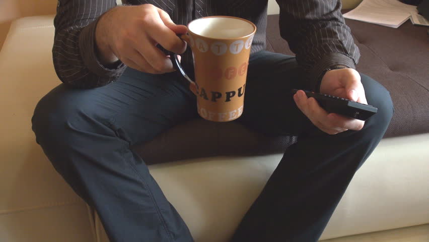 Portrait of modern people, man on living room sofa, drinking coffee, watching TV
