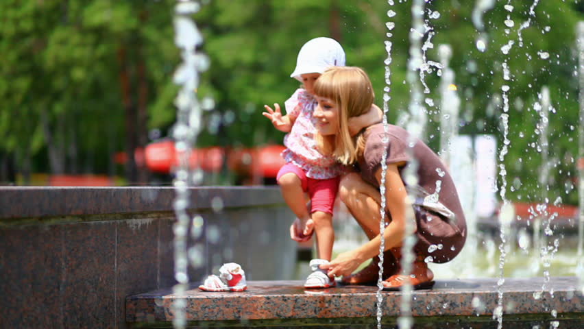 Child and mother in the fountains. Mother takes baby shoes.