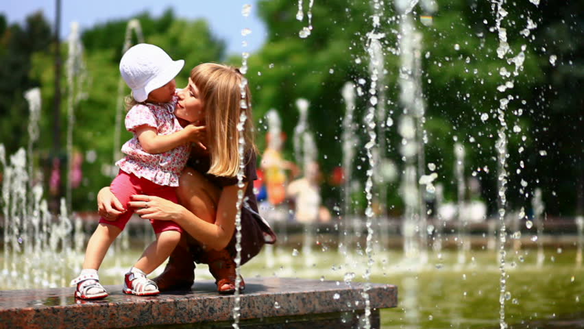 Child and mother in the fountains. They play with water.