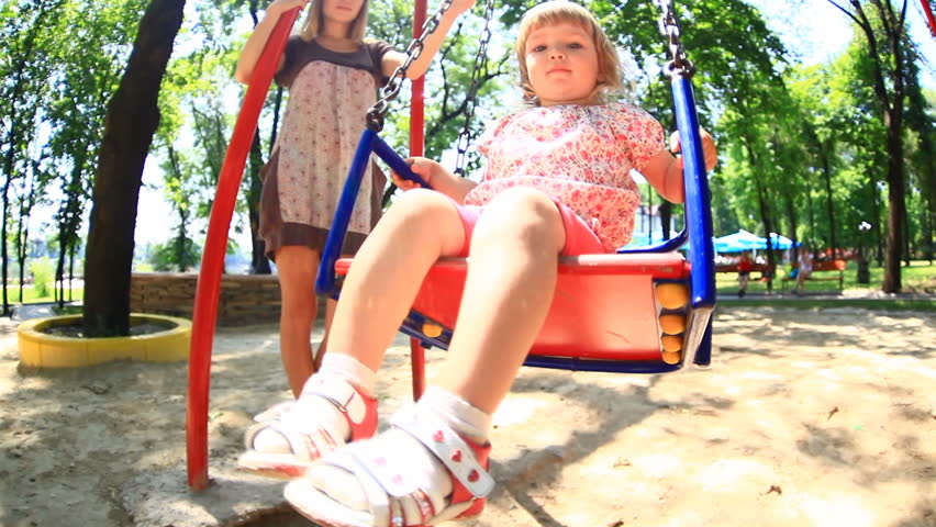 Little girl riding on a swing. Mother stands next