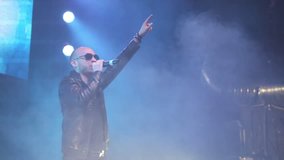 Cool lead singer of music group in sunglasses sings and jumps on stage in night club