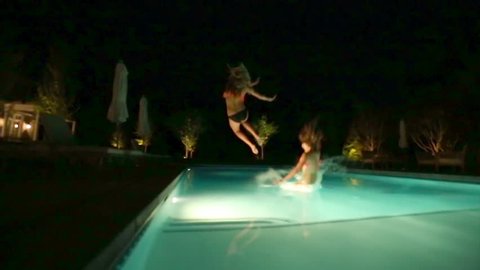 2 Girls Run And Jump Into A Pool At Night (Camera on Dolly)