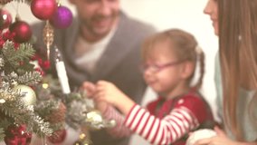 Young happy family-mother father and little daughter decorating Christmas and New Year tree together. Joyful child hanging christmas baubles on fir tree brunch and than clapping. HD video footage 1080