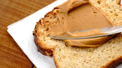 Slow motion macro of spreading creamy peanut butter on low-carb toast