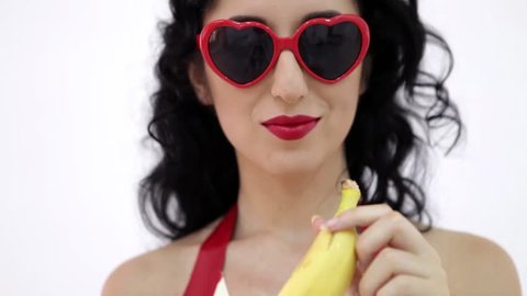 Sexy brunette with red sunglasses eating banana.