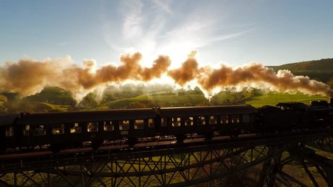 epic aerial view of steam engine train crossing bridge at sunset magic hour. old locomotive