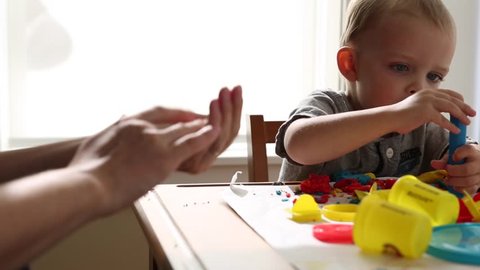 A pregnant mother plays with her toddler boy on a table with clay