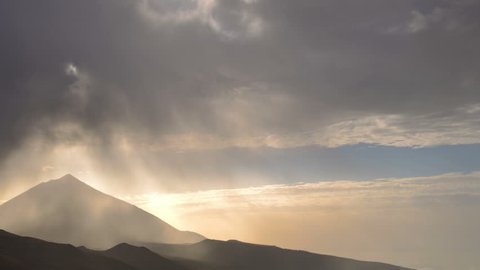 Landscape, stormy clouds over mountains and Teide volcano baclit by setting sun, time-lapse, zoom out.