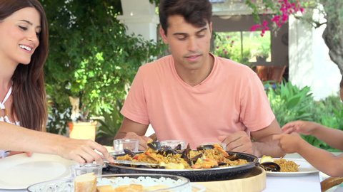 Hispanic mother serves meal of paella as family sit on outdoor terrace. Shot on Sony FS700 at frame rate of 25fps