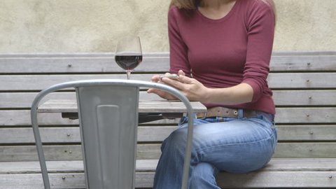 A middle aged woman texting at an outdoor table while enjoying a glass of wine