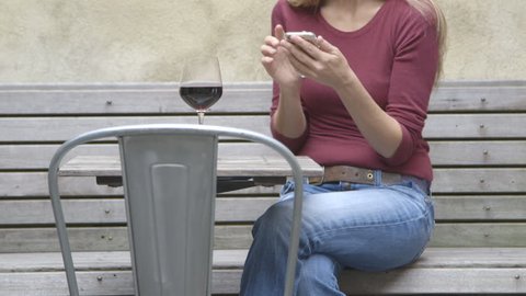 A middle aged woman texting at an outdoor table while enjoying a glass of wine