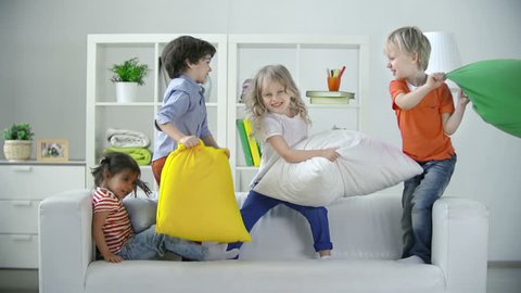 Four kids playing on sofa pillow fighting 