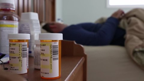 A man lying sick in bed next to his medications in his home