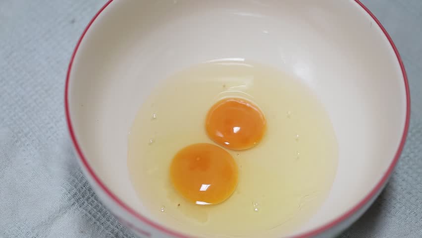Hand cracks a fresh eggs into the bowl