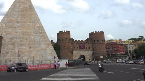ROME - OCT. 2014: Cars pass through Porta San Paolo, zoom in to one almost colliding w motorcycle, past Pyramid of Cestius, or Piramide, built circa 18 BCE –12 BCE.  Museo della Via Ostiense in castle
