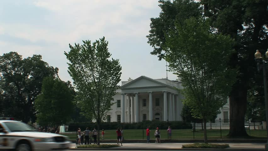 Wide Shot of White House north side as US Secret Service Uniformed Division marked cruiser drives by.  Tourists walk by on Pennsylvania Ave.   Summertime.  