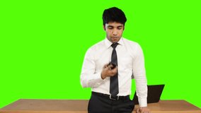Locked-on shot of a young businessman talking on mobile phone against green background
