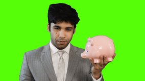 Locked-on shot of a young businessman inserting money into a piggy bank on green background
