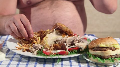 Hungry overweight man eating fried chicken with french fries at home