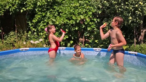 Happy boy and two girls play sticky tennis in swimming pool in summer garden