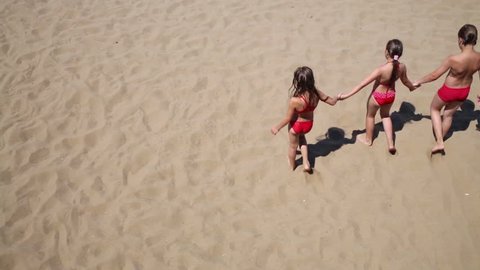 Back of boy and two little girls holding hands walking on yellow sand of beach