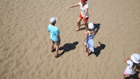 Mother with three children play blindman buff on yellow sand of beach