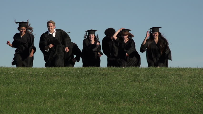 A slow motion mid-shot of a group of racially-diverse graduation students running over a hill, jumping into the air in triumph and throwing their mortarboards.