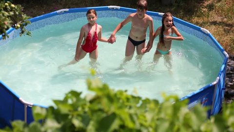 Three happy children jump in swimming pool in summer garden