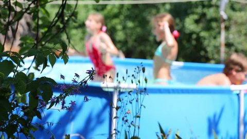 Three happy children play in swimming pool in summer garden. Focus on wildflower