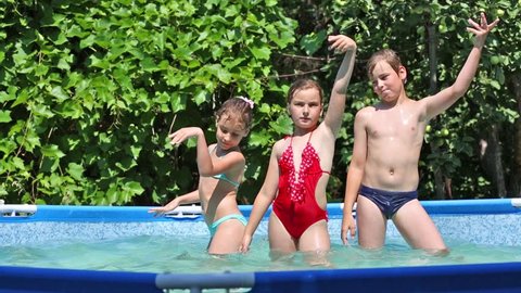 Boy and two girls dance in swimming pool in summer garden