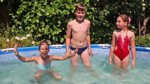 Happy boy and two girls jump and splash in swimming pool in garden