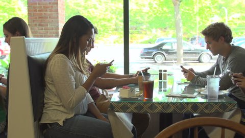A dolly across four, racially-diverse, friends, all using their cell phones at a restaurant table. Property released