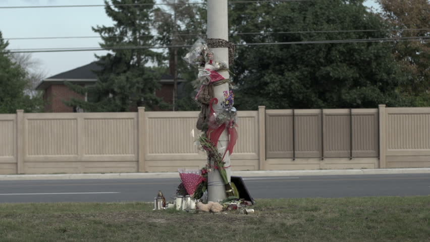 A time lapse shot of a road accident memorial on the side of a road, as cars rush past at great speed.